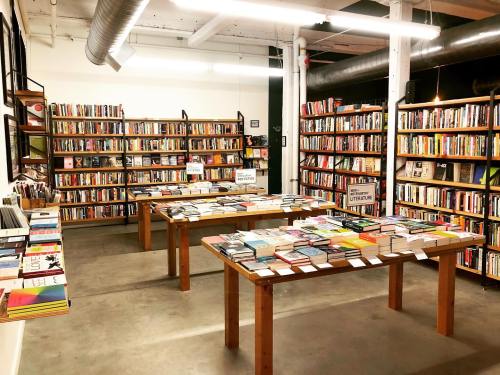 A cozy bookstore interior with wooden tables displaying books and shelves filled with various titles.