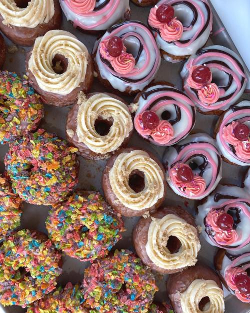 A tray of colorful donuts, including frosted, fruity, and cream-filled varieties, topped with cherries and cereal.