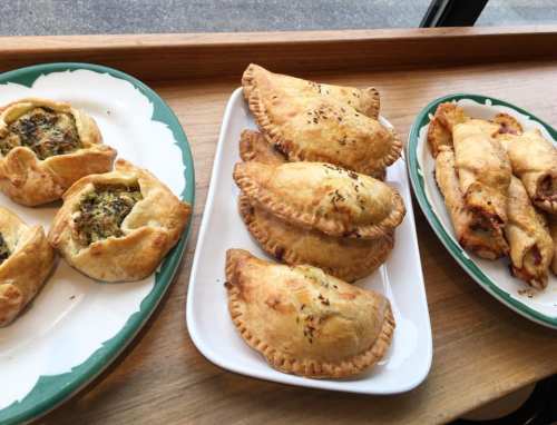 A display of savory pastries on plates, including stuffed empanadas and flaky pastries with various fillings.