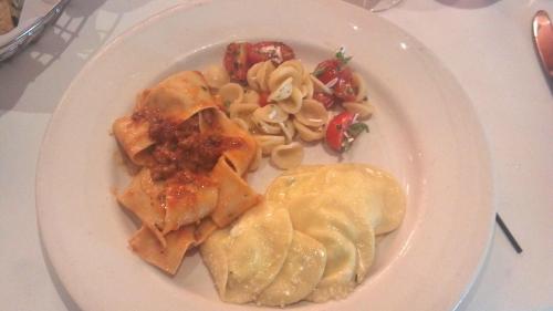 A plate of pasta featuring pappardelle with meat sauce, orecchiette with tomatoes, and cheese-filled ravioli.