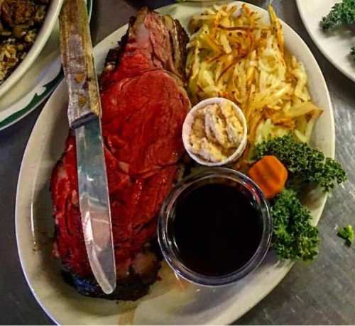 A plate featuring a large slice of roast beef, hash browns, coleslaw, a dipping sauce, and a side of kale.