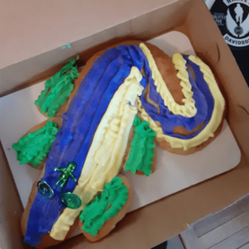 A colorful cake shaped like a river, decorated with green and purple icing, and topped with a small toy figure.
