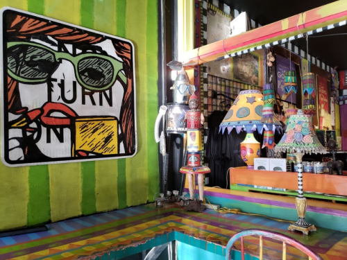 Colorful interior of a quirky cafe featuring vibrant wall art, a unique lamp, and eclectic decor.