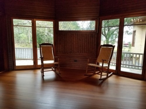 Two wooden rocking chairs facing each other in a room with large windows and wooden walls, overlooking a porch.