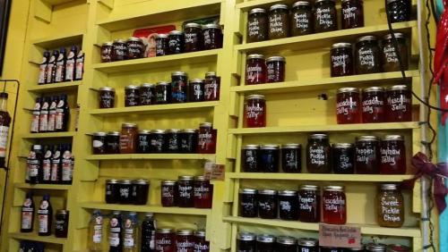 Shelves filled with jars of colorful jams, jellies, and pickles against a bright yellow background.