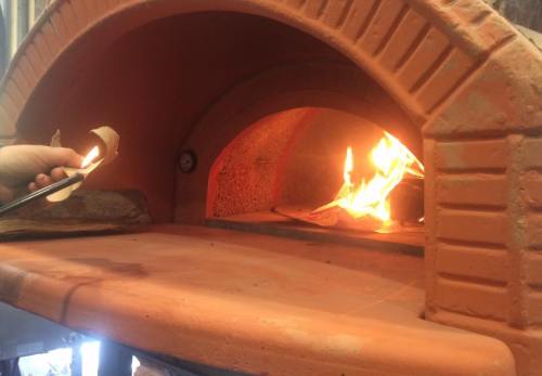 A hand holding a piece of paper is igniting a fire inside a brick oven. Flames are visible inside the oven.