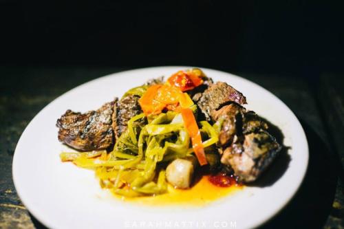 A plate of grilled meat served with sautéed greens and red peppers, garnished with a tangy sauce.