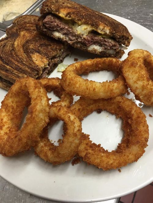 A plate with crispy onion rings and a grilled sandwich filled with meat and cheese, partially cut in half.