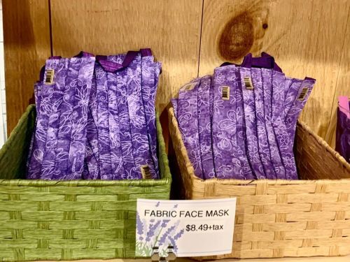 Two baskets filled with purple fabric face masks, displayed with a sign indicating the price of $8.49 plus tax.