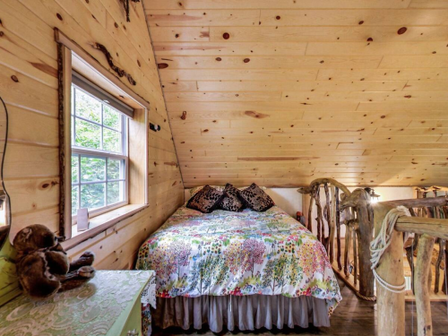 Cozy attic bedroom with a wooden ceiling, floral bedding, and a window letting in natural light.