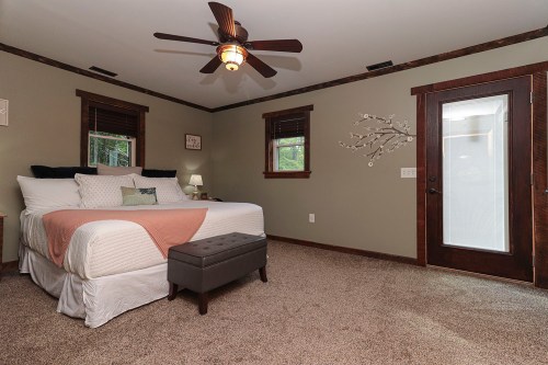 Cozy bedroom with a queen bed, ceiling fan, and a door leading outside, featuring warm green walls and carpeted floor.