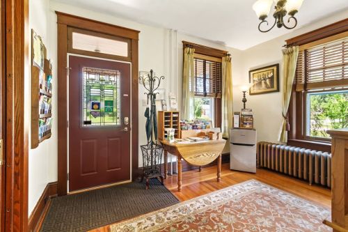 Cozy entryway with a stained glass door, wooden furniture, and large windows, featuring a rug and radiator.