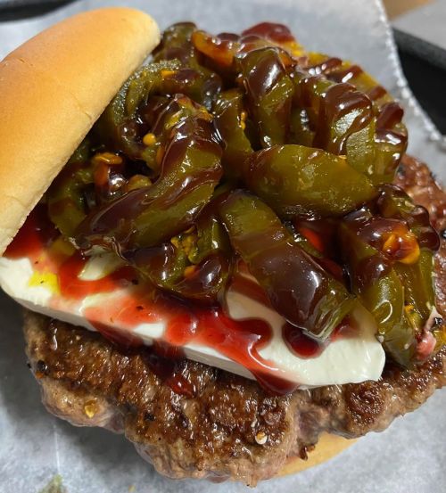 A close-up of a hamburger with a beef patty, mayonnaise, ketchup, and a generous topping of green peppers.