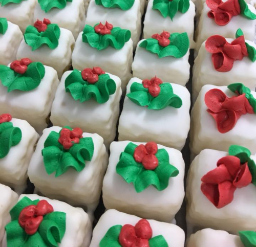 A close-up of festive mini cakes decorated with white icing, green holly leaves, and red berries.
