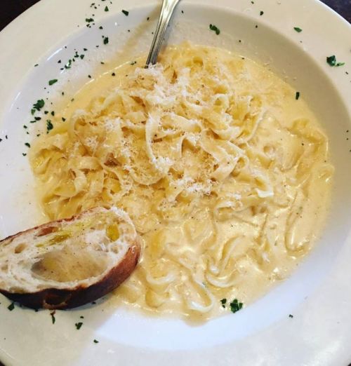 A plate of creamy fettuccine pasta topped with grated cheese, accompanied by a slice of bread.
