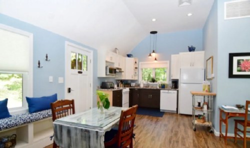 Bright kitchen with blue walls, white cabinets, a dining table, and a cozy seating area by the window.
