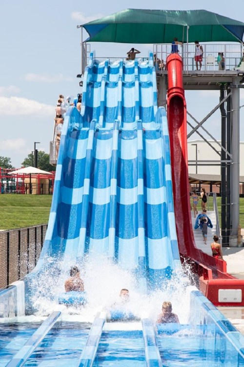 A water park with two large slides, one blue and one red, as people splash into the pool below.