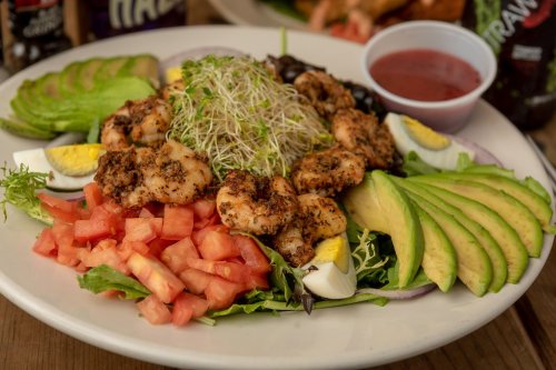A vibrant salad with seasoned shrimp, avocado, tomatoes, hard-boiled eggs, sprouts, and a side of dressing.