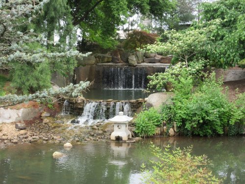 A serene garden scene featuring a waterfall, lush greenery, and a stone lantern by a tranquil pond.