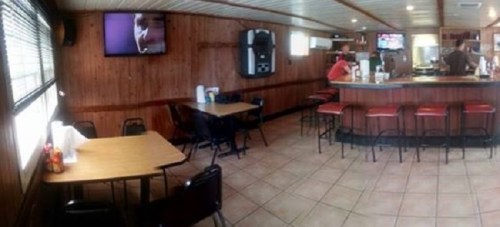 A cozy diner interior with wooden walls, tables, and a bar area; TVs are mounted on the walls.