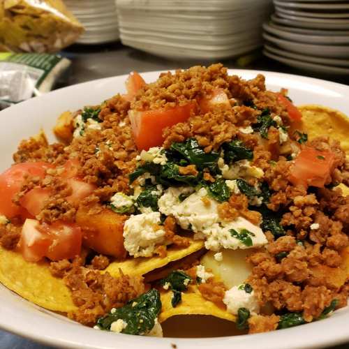 A bowl of nachos topped with crumbled meat, tomatoes, spinach, and cheese.