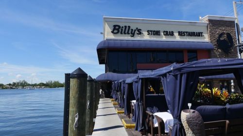 Exterior of Billy's Stone Crab Restaurant by the water, featuring outdoor seating and a clear blue sky.
