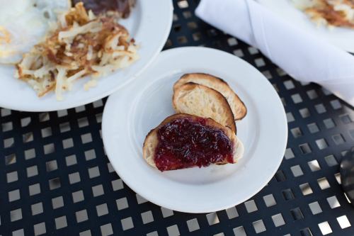 A plate with toasted bread topped with jelly, next to a plate of hash browns on a black table.
