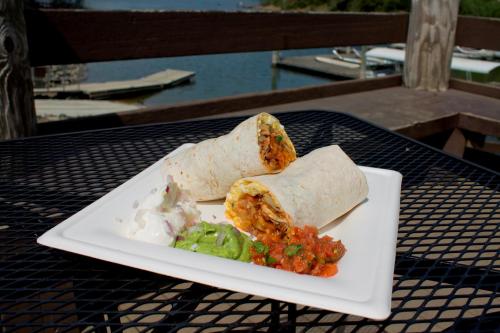 Two burritos on a plate with salsa, guacamole, and sour cream, set on a table by a waterfront.