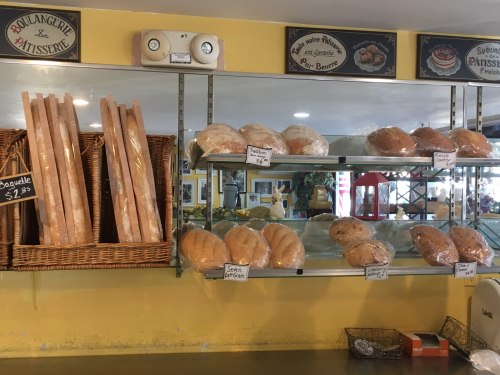 A bakery display featuring various loaves of bread on shelves and in baskets, with price tags visible.
