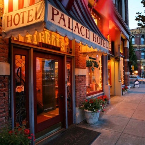 Historic hotel entrance with a striped awning, flower pots, and warm lighting on a charming street.