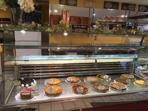 A display case filled with various desserts, including cakes and tarts, with labels and decorative flowers.