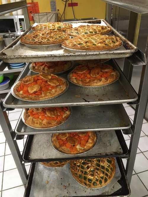 A metal rack filled with various pies, including fruit and vegetable fillings, in a kitchen setting.
