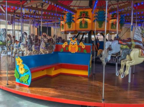 Colorful carousel with ornate horses and a vibrant seating area featuring an owl design and floral decorations.