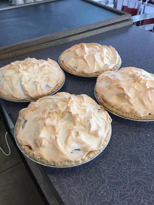 Four freshly baked pies with golden meringue topping on a countertop.