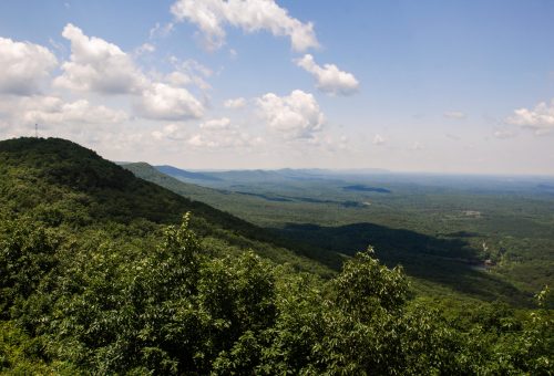 A panoramic view of lush green mountains under a blue sky with fluffy white clouds.