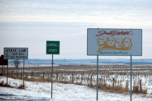 Road signs in a snowy landscape, including a South Dakota welcome sign and a seat belt law reminder.