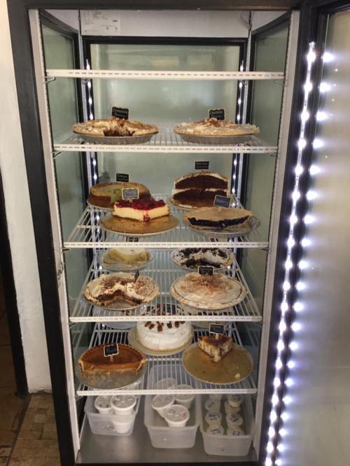 A display case filled with various cakes and desserts, including pies and cheesecakes, on multiple shelves.