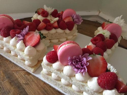 A beautifully decorated cake with layers, topped with strawberries, raspberries, macarons, and edible flowers.
