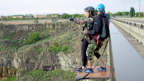 A person prepares to bungee jump off a platform, with a harness and helmet, overlooking a rocky canyon.