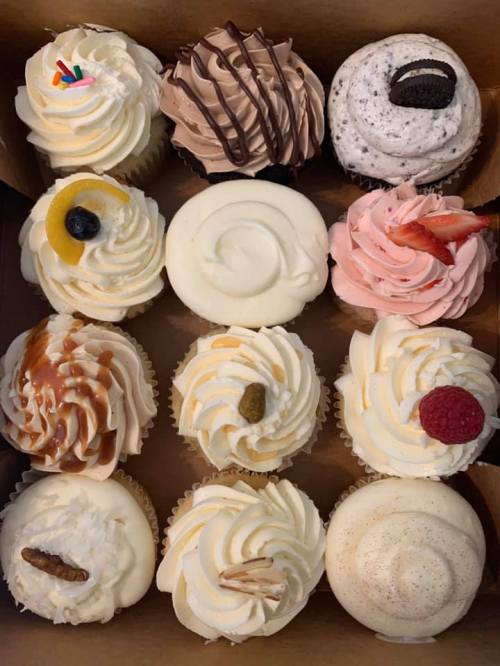 A box of twelve assorted cupcakes with various toppings and flavors, including chocolate, fruit, and caramel.
