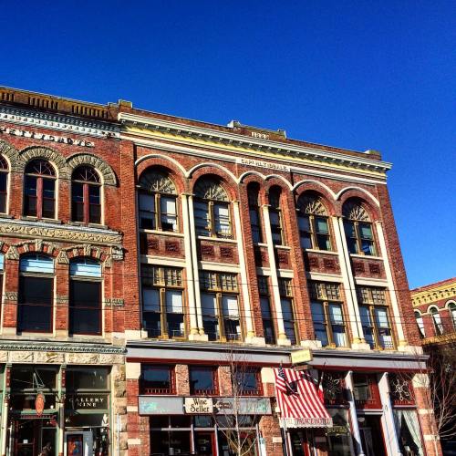 Historic brick building with arched windows, decorative details, and an American flag in front against a clear blue sky.