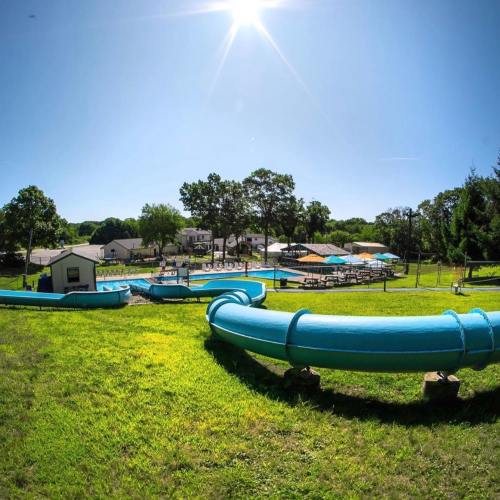 A sunny day at a water park featuring blue slides and a pool area surrounded by green grass and trees.