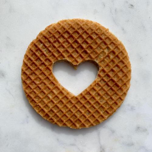 A round waffle cookie with a heart-shaped cutout in the center, resting on a marble surface.
