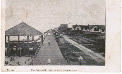 Black and white image of a boardwalk in Rehoboth, Delaware, with houses and a gazebo along the path.