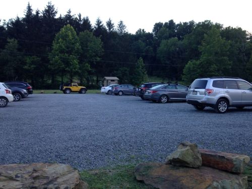 A gravel parking lot with several parked cars and trees in the background, under a clear sky.