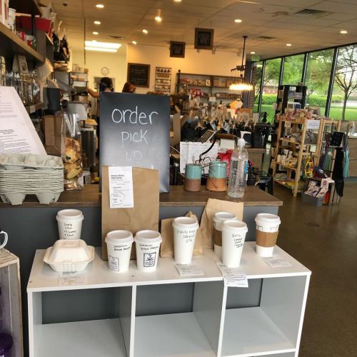 A cozy café interior with a counter, coffee cups on display, and a sign for order pickup.
