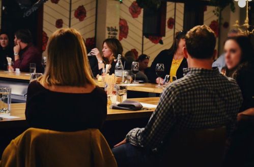 A group of people seated at a bar, with a focus on two individuals in the foreground, enjoying a social gathering.