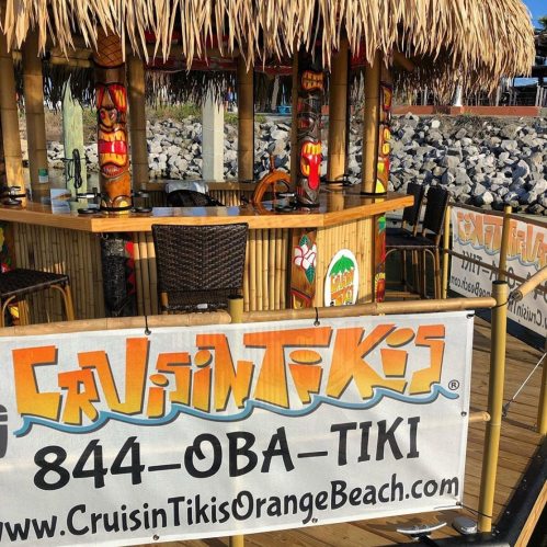 A tiki bar with a thatched roof, colorful decor, and a sign displaying "Cruisin' Tikis" and contact information.
