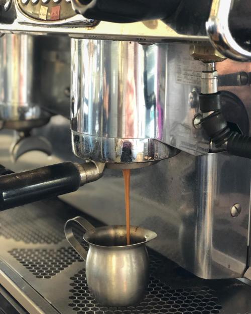 A close-up of an espresso machine pouring coffee into a small metal pitcher.