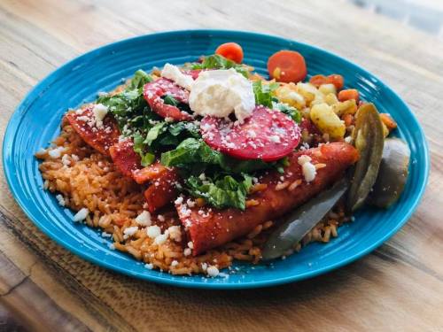 A vibrant plate of enchiladas topped with lettuce, tomatoes, sour cream, served with rice and mixed vegetables.